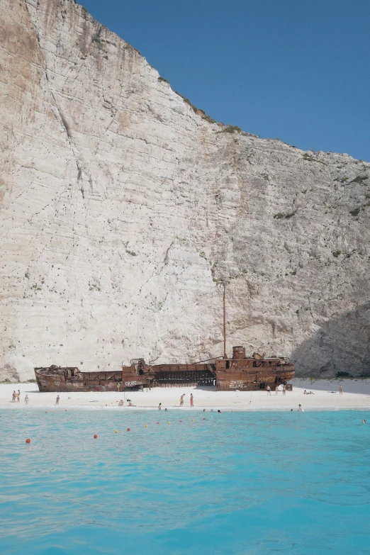 a boat sitting on top of a sandy beach next to a cliff, inspired by Thomas Struth, minimalism, greek pool, an impossibly huge pirate ship, low quality photo, chalk cliffs above