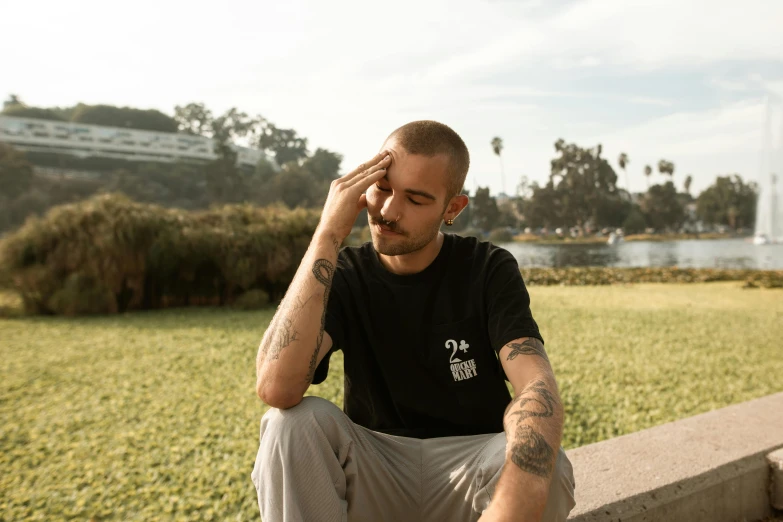 a man sitting on a bench in front of a fountain, inspired by Seb McKinnon, unsplash, realism, black t shirt, lil peep, meditating pose, chilled out smirk on face