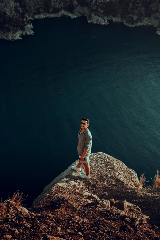 a man standing on top of a rock next to a body of water, looking down on the camera, manly, quixel megascans, young man