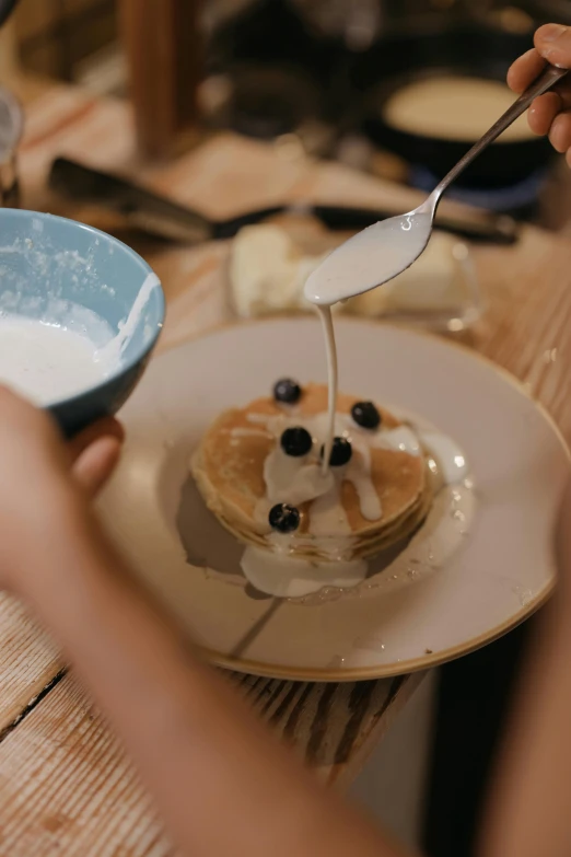 a person sitting at a table with a plate of food, pancakes, filling the frame, cream of the crop, indigo