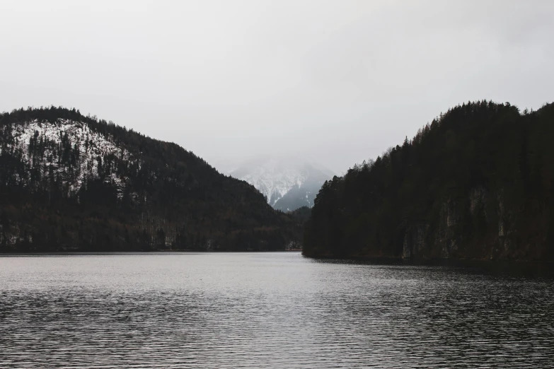 a body of water with mountains in the background, by Emma Andijewska, pexels contest winner, romanticism, grey forest background, slight overcast weather, a cold, snapchat photo