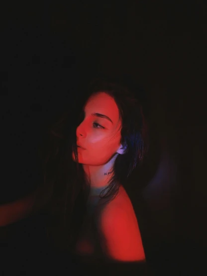 a woman standing in the dark with a red light on her face, inspired by Elsa Bleda, pexels contest winner, aestheticism, soft devil queen madison beer, young glitched woman, ☁🌪🌙👩🏾, portait photo profile picture