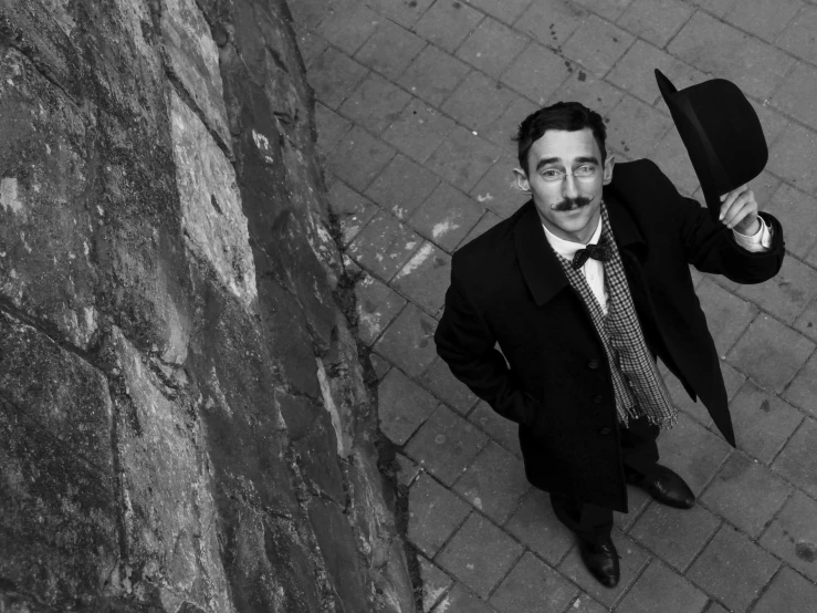 a man in a suit and tie holding a hat, a photo, inspired by Henri Cartier-Bresson, long twirling moustache, clothed in ancient street wear, tim burton, standing with a parasol