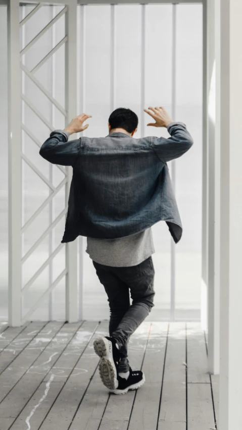 a man walking down a hallway with his back to the camera, an album cover, inspired by Fei Danxu, pexels contest winner, altermodern, jump pose, gray shirt, cardigan, ignant