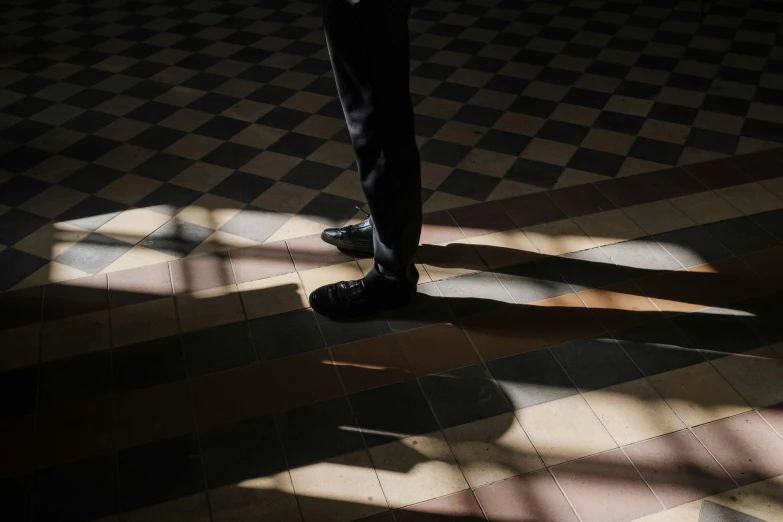 a person standing in a room with a checkered floor, inspired by Vivian Maier, unsplash, dappled lighting, focus on his foot, schools, silhouetted