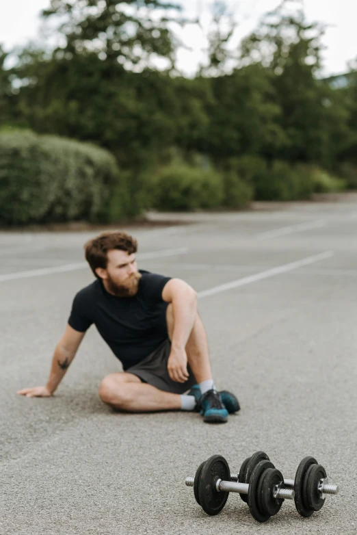 a man sitting on the ground next to a pair of dumbbells, by Daniel Seghers, pexels contest winner, running sequence, tired half closed, outside, 30 year old man :: athletic