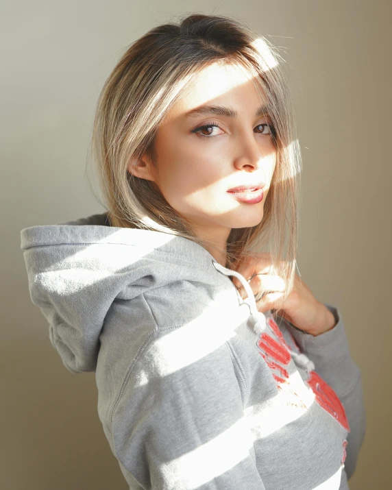 a woman in a hoodie poses for a picture, inspired by Elsa Bleda, trending on pexels, photorealism, soft grey and red natural light, glam photo, basia tran, sunny lighting