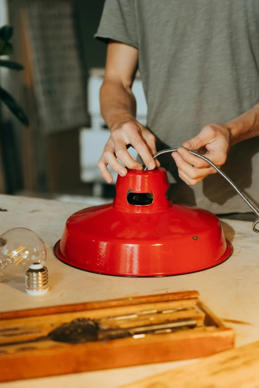 a man is working on a red lamp, trending on pexels, metal lid, holding electricity, restomod, full colour