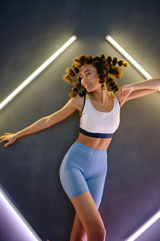 a woman standing in front of a wall with neon lights, trending on pexels, renaissance, sport bra and dark blue shorts, dynamic hair movement, soft lighting from above, curated collections