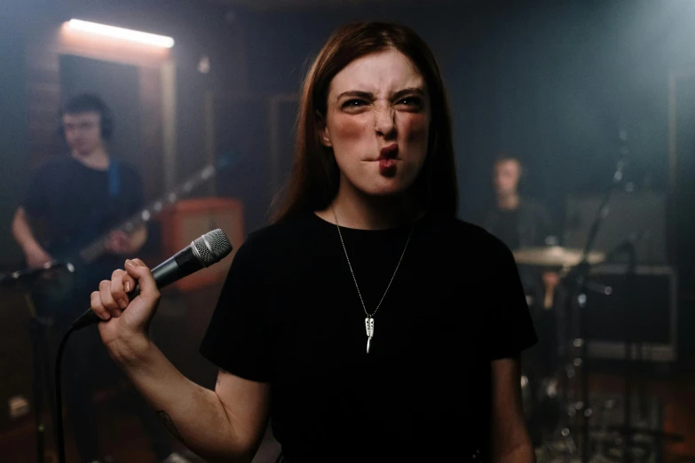 a woman standing in front of a microphone, pexels contest winner, antipodeans, pout, hozier, holding it out to the camera, rock band