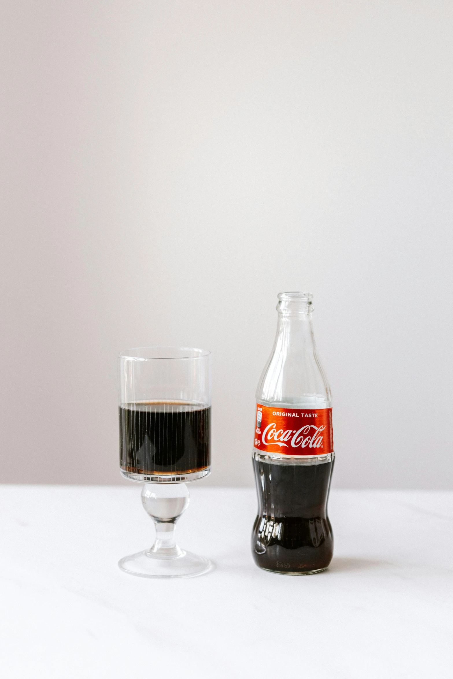 a bottle of coke next to a glass of coke, inspired by Dorothy Coke, frontal shot, on clear background, small, wine glass