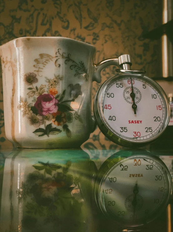 a clock sitting on top of a table next to a cup, a cross stitch, pexels contest winner, hyperrealism, vintage closeup photograph, ((oversaturated))