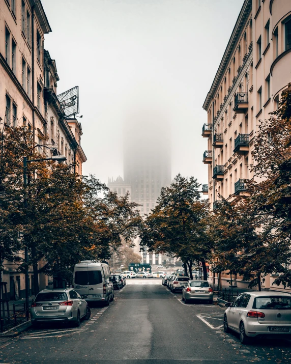 a street lined with parked cars and tall buildings, by Emma Andijewska, unsplash contest winner, slight fog, berghain, trees in background, non-binary