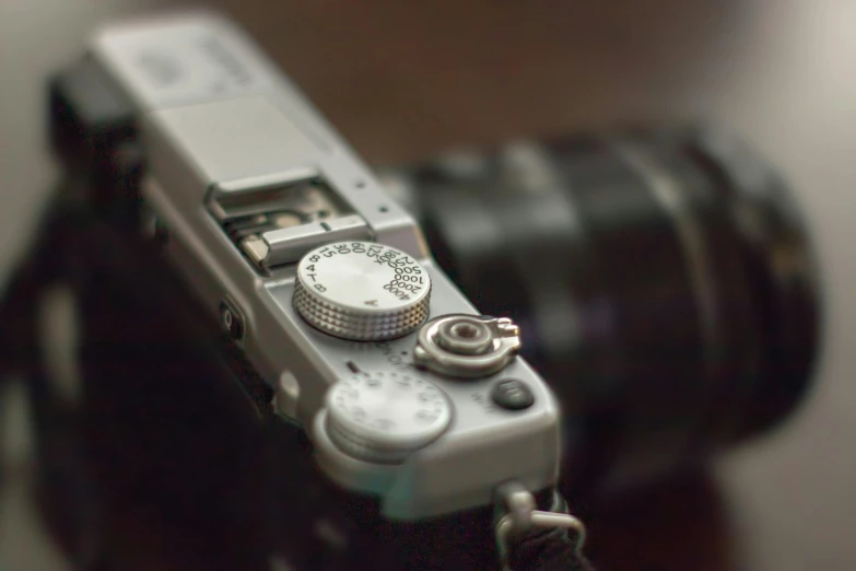a silver camera sitting on top of a wooden table, by David Simpson, unsplash, photorealism, blurred detail, dials, fujifilm”, anime shot