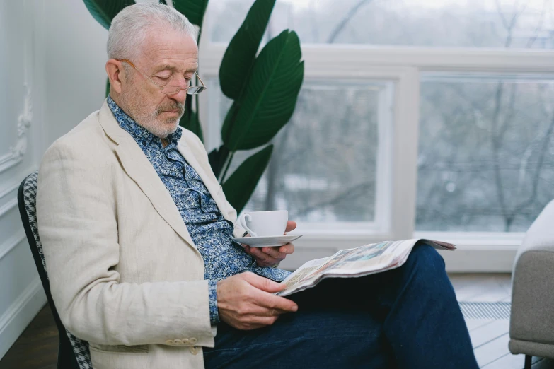 a man sitting in a chair reading a newspaper, a photo, by Will Ellis, pexels contest winner, short white beard, with a white mug, avatar image, casually dressed