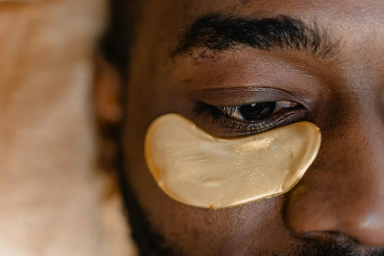 a man with a gold eye patch on his face, trending on pexels, afrofuturism, skin care, behind the scenes photo, smooth waxy skin, detailed body and eyes