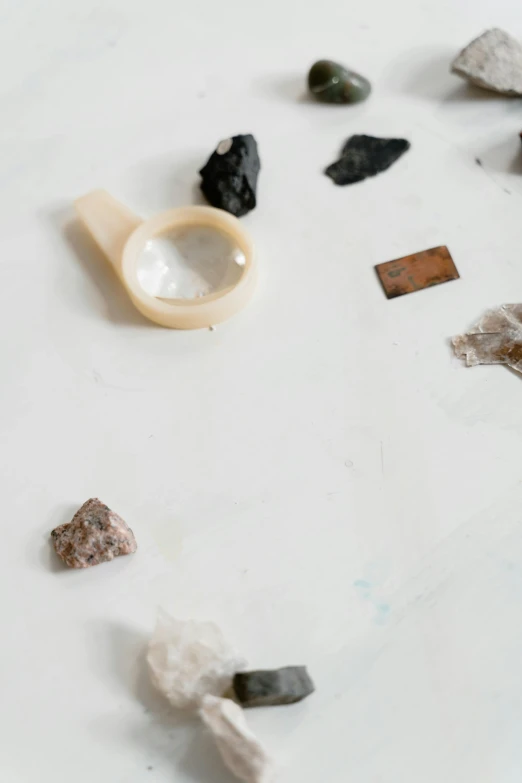 a close up of rocks and stones on a table, by Rebecca Horn, unsplash, assemblage, on a white background, magnifying glass, ashes crystal, julia hetta