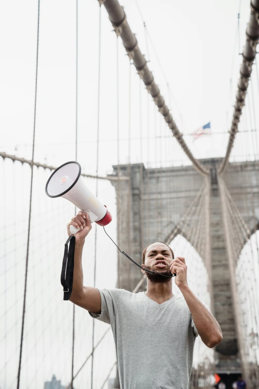 a man standing on top of a bridge holding a megaphone, pexels contest winner, black arts movement, new york times, 🚿🗝📝, strong young man, patriotism