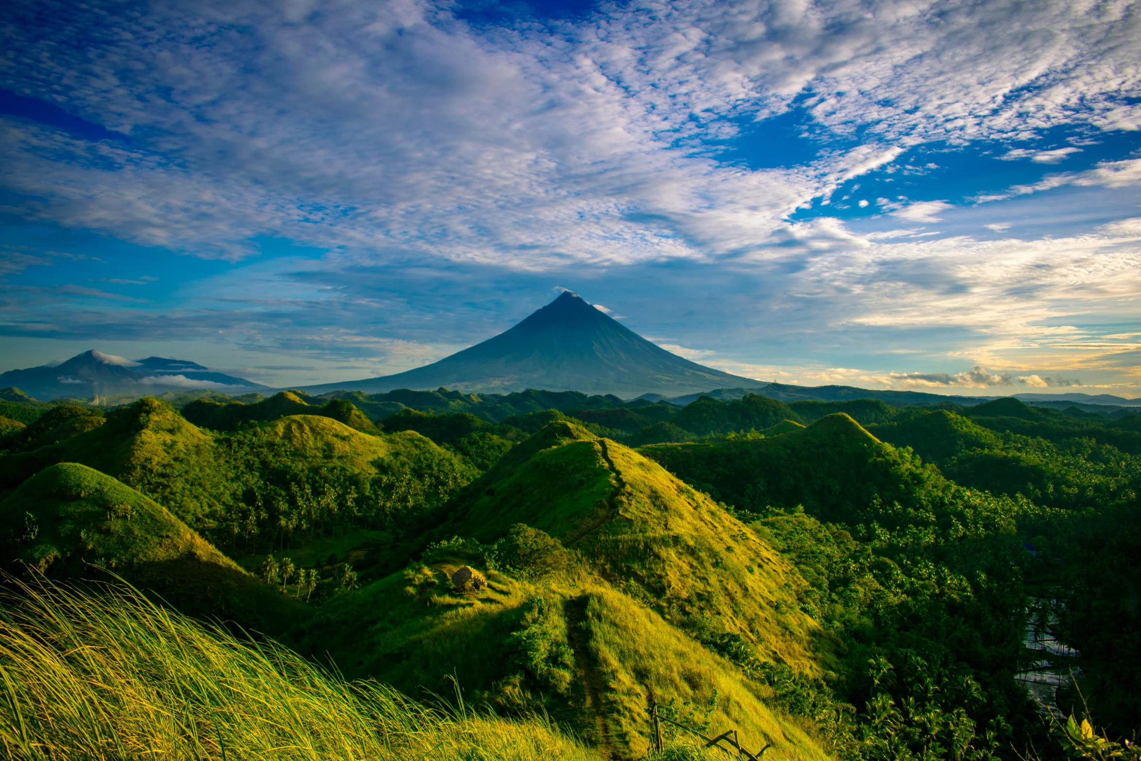 a mountain covered in green grass next to a lush green forest, by Matt Cavotta, pexels contest winner, sumatraism, with a volcano in the background, avatar image, philippines, conde nast traveler photo