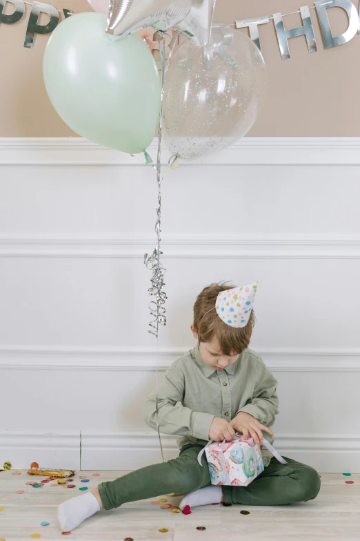 a little girl sitting on the floor with balloons and confetti, a colorized photo, green hat, boy with neutral face, illustration:.4, jellycat