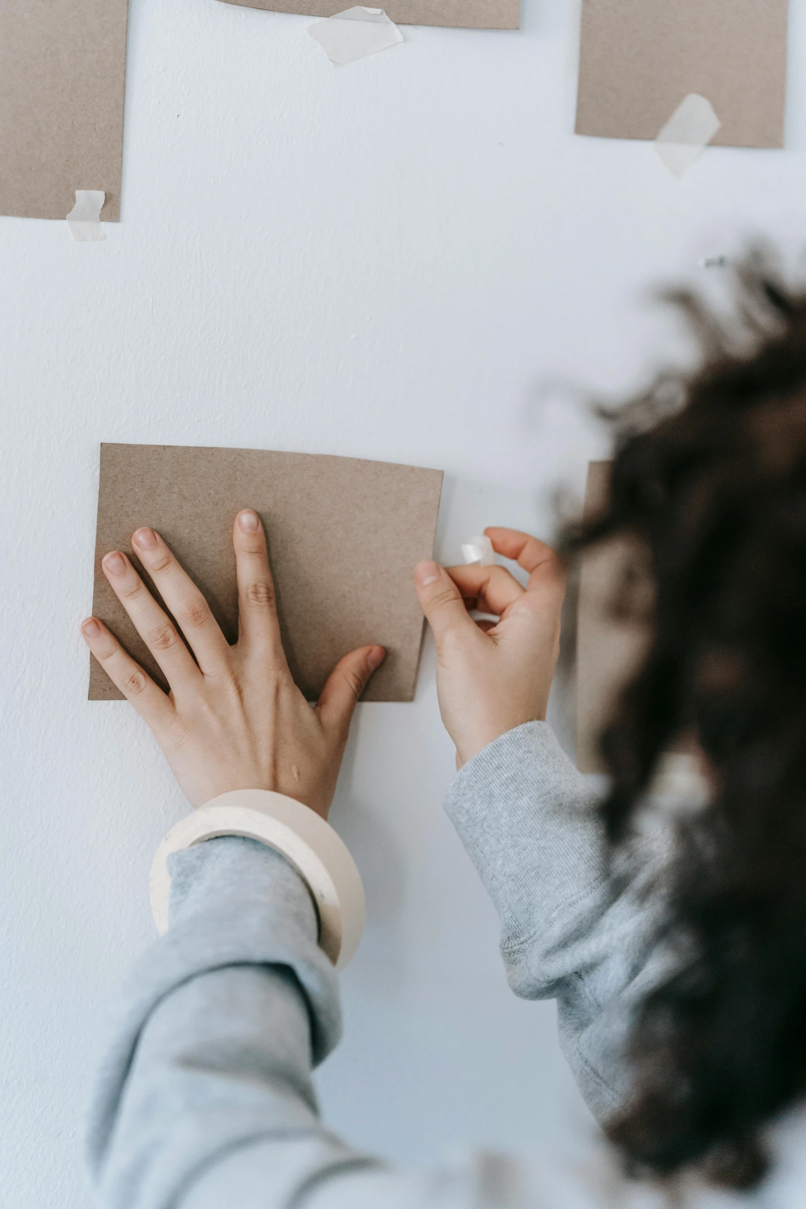 a woman placing a piece of paper on a wall, a child's drawing, by Jessie Algie, pexels contest winner, visual art, brown paper, square shapes, playing cards, on a white table