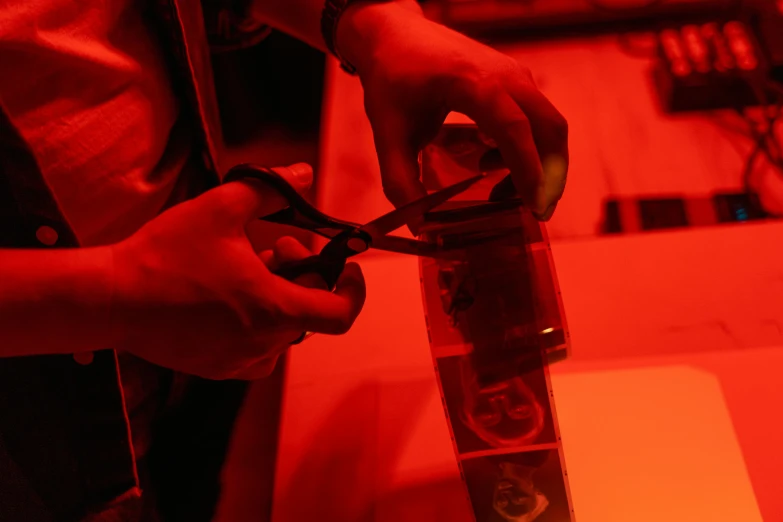 a person cutting a piece of paper with a pair of scissors, by Adam Marczyński, pexels contest winner, process art, glowing jar, red light, handling laboratory equipment, thumbnail