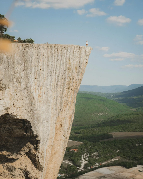 a person standing on top of a cliff, by Tamas Galambos, pexels contest winner, limestone, viewed from a distance, beth cavener, a gigantic wall