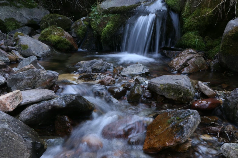 a small waterfall flowing through a lush green forest, by Mirko Rački, unsplash, hurufiyya, medium format. soft light, rocks, brown, 2000s photo