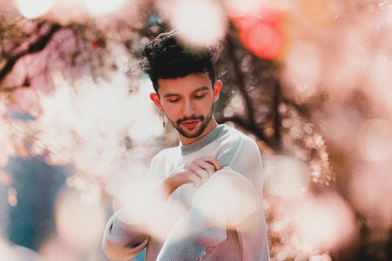 a man standing in front of a flowering tree, an album cover, pexels contest winner, antipodeans, he is wearing a brown sweater, pastel clothing, sayem reza, 50 mm bokeh