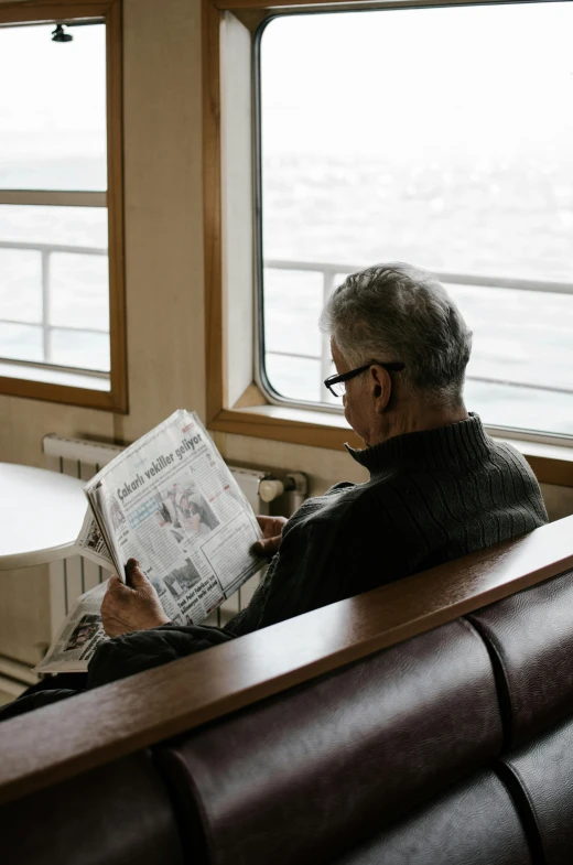 a man sitting on a couch reading a newspaper, by Sebastian Spreng, pexels contest winner, inside large window of ship, gray haired, nordic, 1 2 9 7