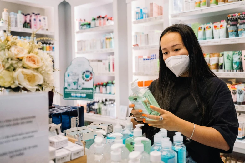 a woman wearing a face mask in a store, by Nicolette Macnamara, pexels contest winner, hurufiyya, pharmacy, toothpaste refinery, manuka, carrying a bottle of perfume