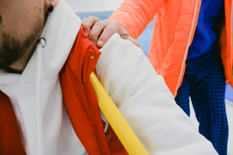 a couple of people standing next to each other, trending on pexels, orange jacket, closeup of arms, plastic and fabric, yellow and red