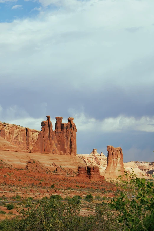 a large rock formation in the middle of a desert, three towers, red cloud, high arches, in a row