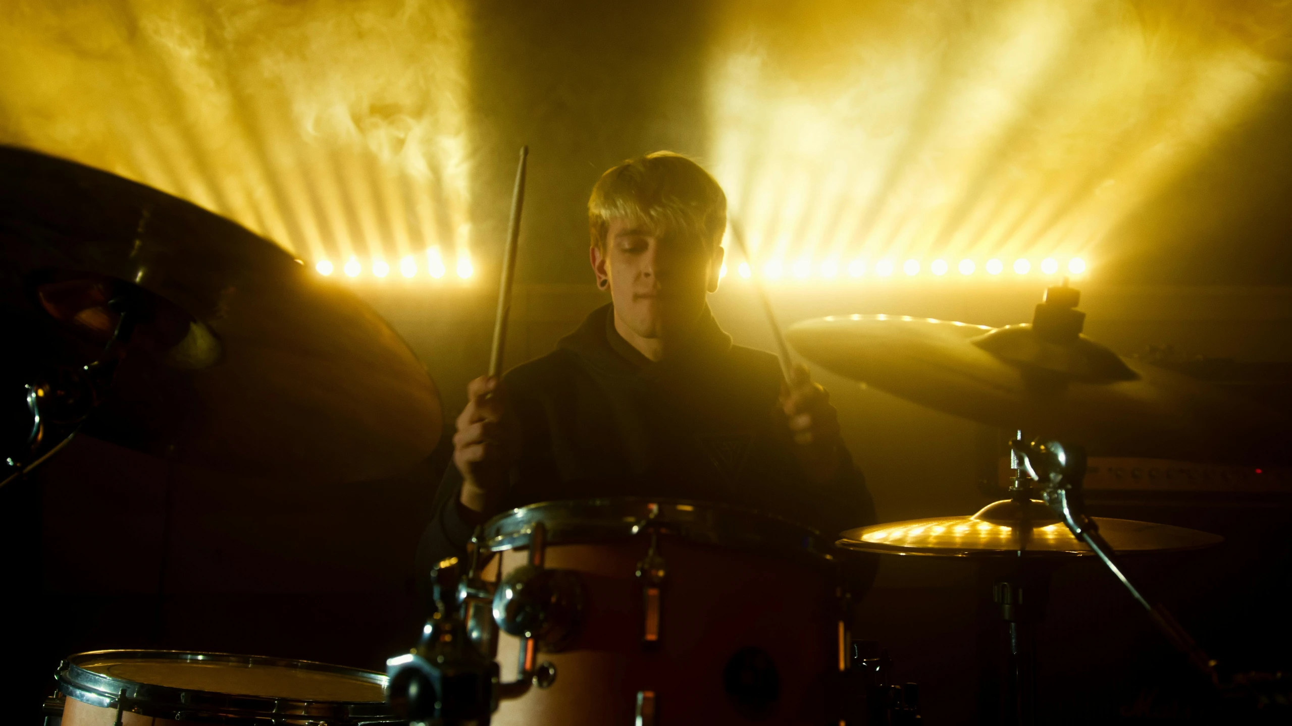 a man playing drums in a dimly lit room, inspired by roger deakins, a blond, yung lean, movie still 8 k, yellow lighting from right