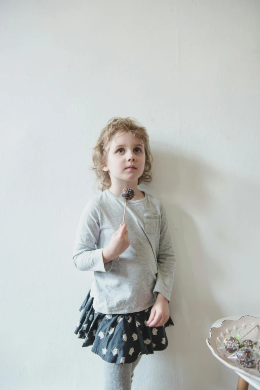 a little girl standing in front of a white wall, by Nina Hamnett, unsplash, visual art, dressed in a gray, wearing a cardigan, like a catalog photograph, young harpy-girl