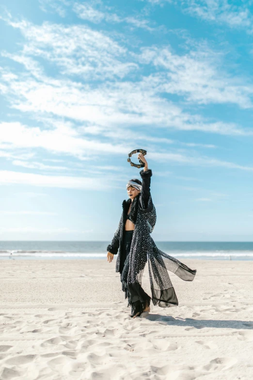 a woman standing on top of a sandy beach, an album cover, unsplash, arabesque, waving robe movement, long black crown, award winning fashion photo, performing