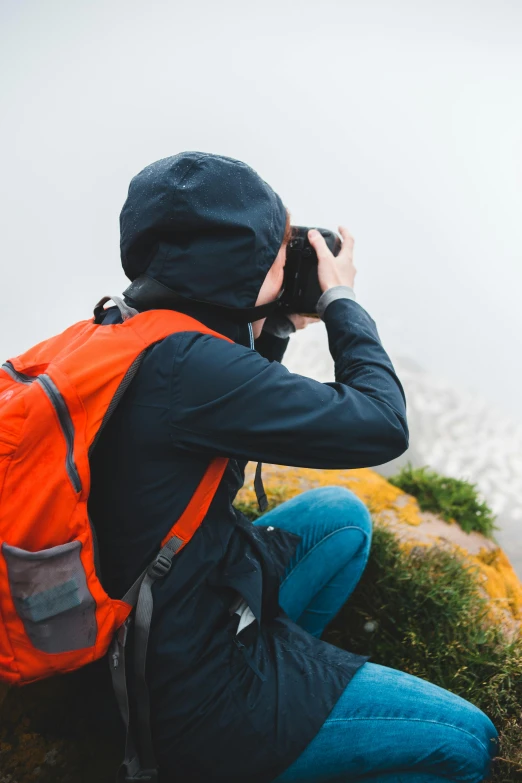 a man sitting on top of a mountain holding a camera, spying discretly, with a backpack, 2019 trending photo, full frame image