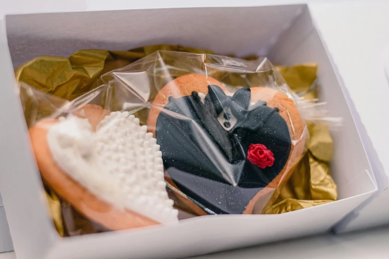 a close up of a box of doughnuts on a table, by Lee Loughridge, pexels contest winner, romanticism, rose gold heart, black, bride and groom, cookies
