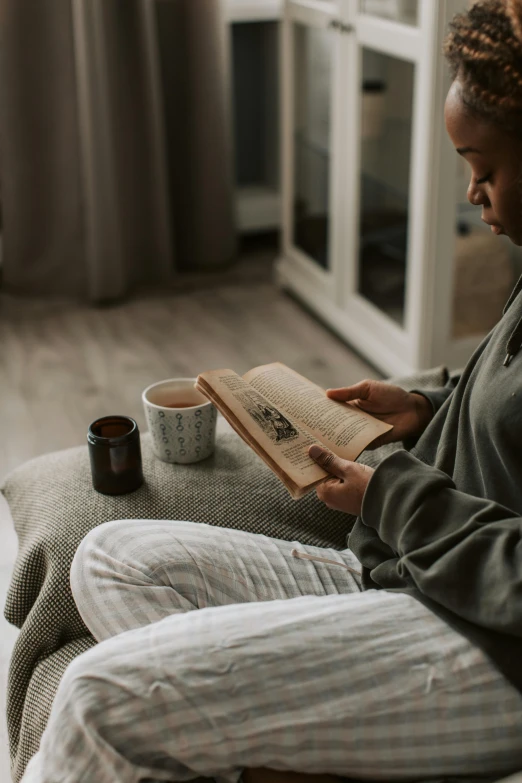 a woman sitting on a couch reading a book, by Adam Marczyński, pexels contest winner, wearing a grey robe, sitting on a mocha-colored table, gif, unedited