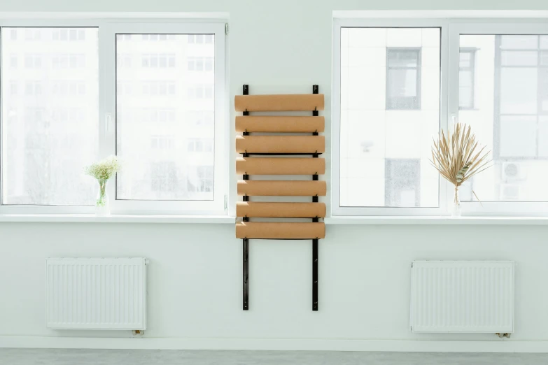 a chair sitting in front of a window next to a radiator, an album cover, inspired by Sarah Lucas, unsplash, bauhaus, made of cardboard, light - brown wall, product view, bench