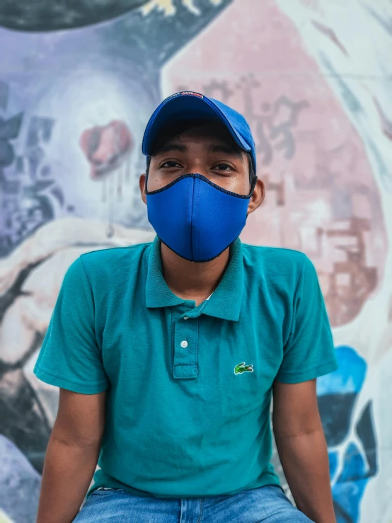 a man sitting in front of a mural wearing a blue mask, by Alejandro Obregón, pexels contest winner, wearing a dark blue polo shirt, gif, low quality photo, boy with neutral face