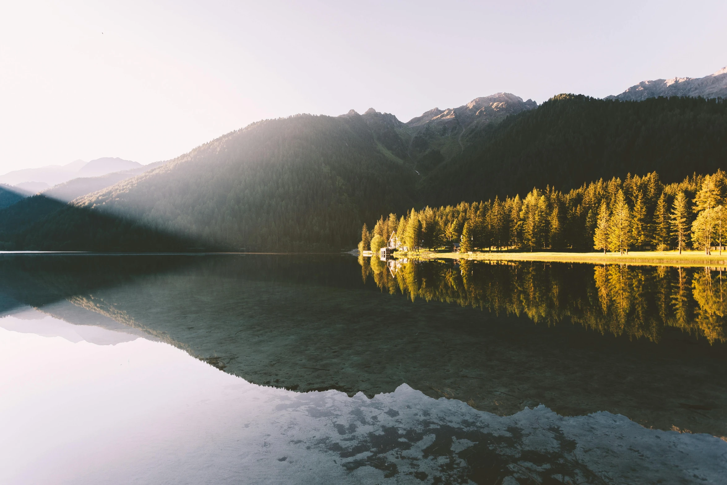 a body of water surrounded by trees and mountains, unsplash contest winner, minimalism, sun flares, multiple stories, filtered evening light, perfect symmetrical image