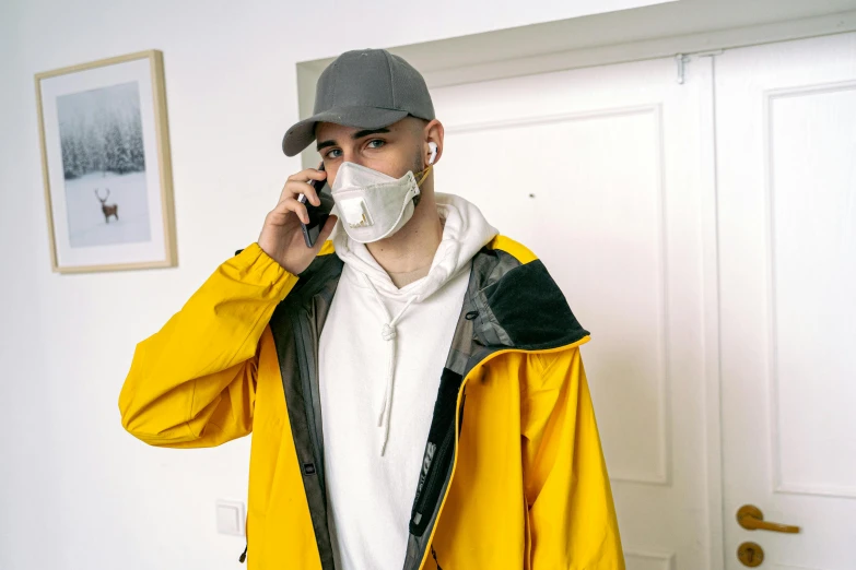 a man in a yellow jacket talking on a cell phone, a photo, inspired by Louis Le Nain, pexels, hyperrealism, medical mask, techwear clothes, zayn malik, in a japanese apartment