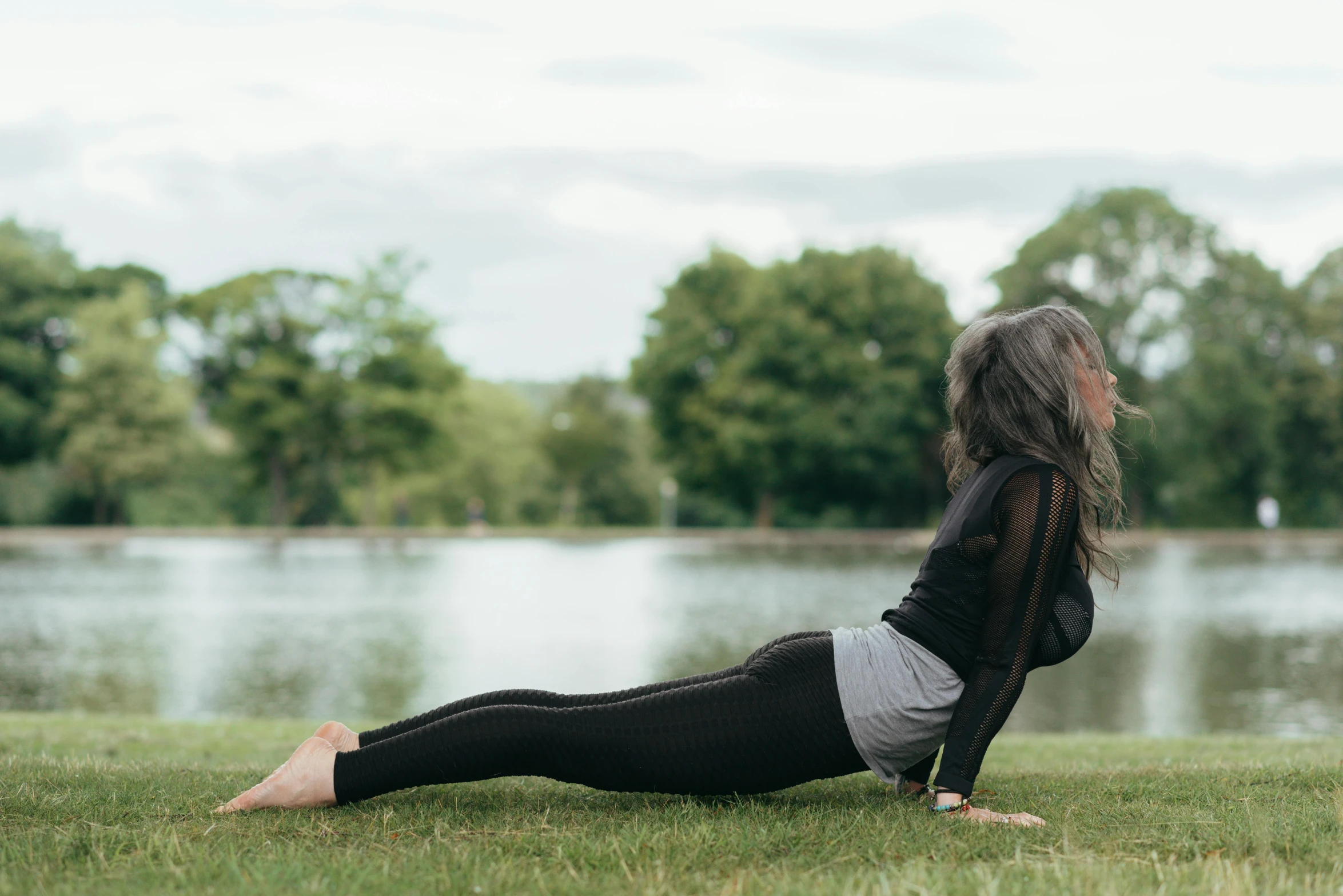 a woman doing a yoga pose in front of a lake, by Rachel Reckitt, arabesque, crawling on the ground, side profile shot, in the park, grey