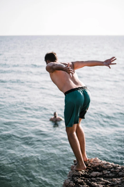a man jumping off a cliff into the ocean, happening, green swimsuit, camaraderie, 2019 trending photo, worried