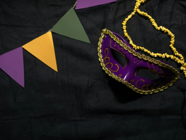 a purple mask sitting on top of a black table, inspired by Bernd Fasching, trending on pexels, renaissance, background image, cloth banners, green and gold