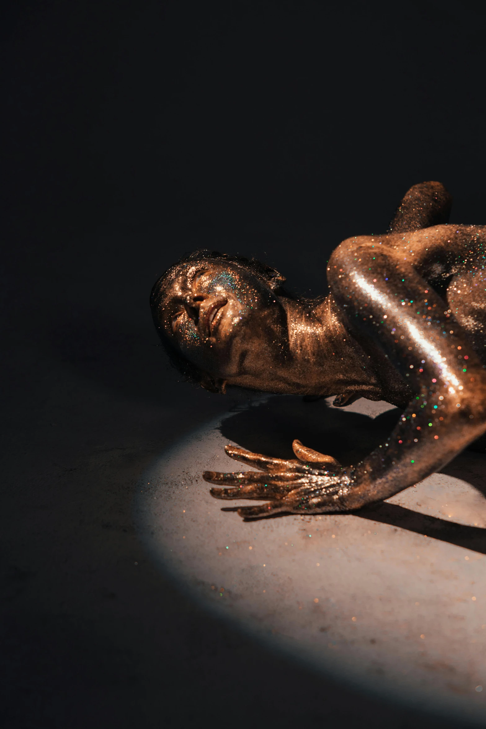 a bronze statue of a man laying on the ground, by artist, trending on unsplash, glittering metal paint, powerful woman sitting in space, performance art, glittering skin