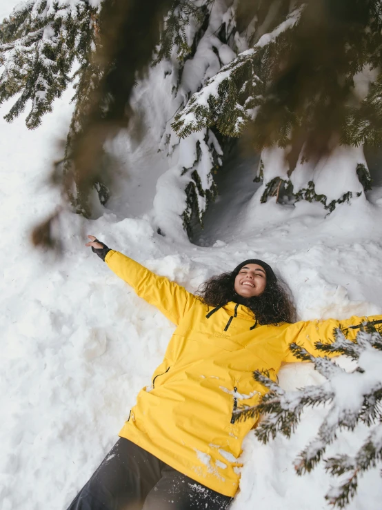 a woman in a yellow jacket laying in the snow, pexels contest winner, arms stretched wide, avatar image, whistler, happy trees