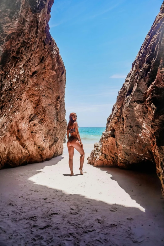 a woman standing in a cave on a beach, white sandy beach, gorgeous features, rock arcs, lush surroundings