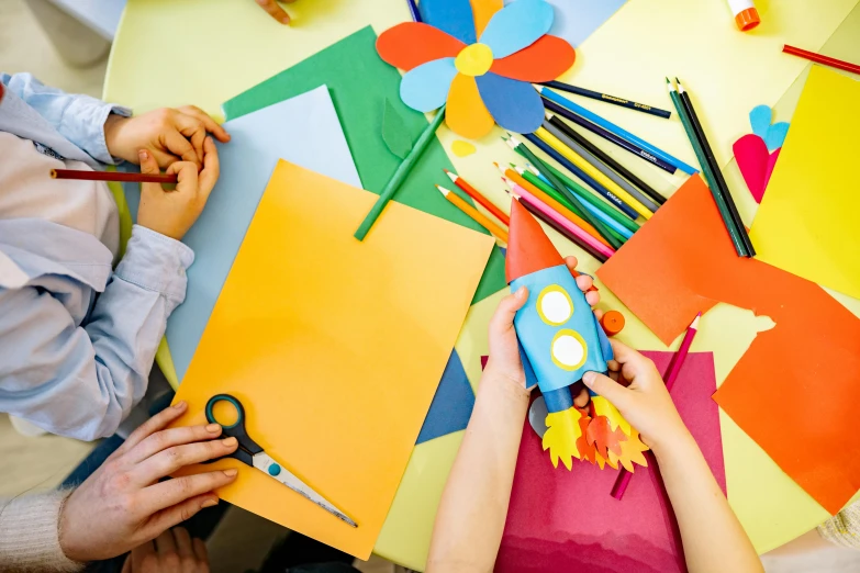 a couple of people that are sitting at a table, a child's drawing, trending on pexels, arts and crafts movement, paper origami flowers, rainbow coloured rockets, school class, thumbnail